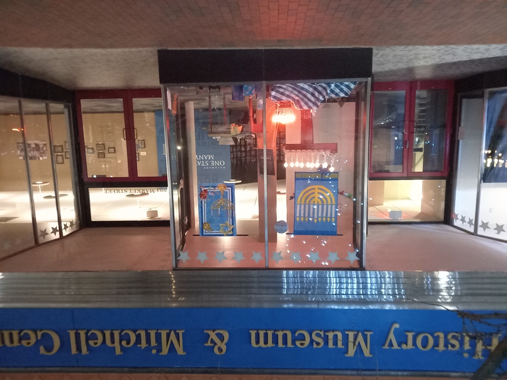 Entrance to the Delaware History Museum and Mitchell Center for African American Heritage at 540 N Market St. Store window decorated with Hanukkah items, hanukkiot, a table with latke ingredients, presents wrapped in Hanukkah-themed paper.